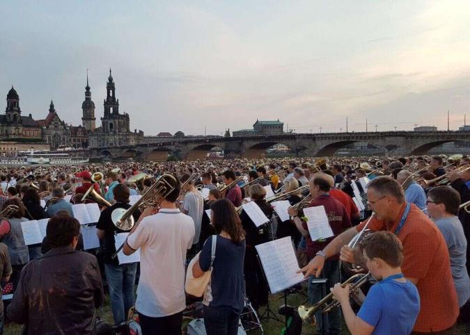 Ein großer Posaunenchor spielt am Elbufer in Dresden während der Dämmerung.