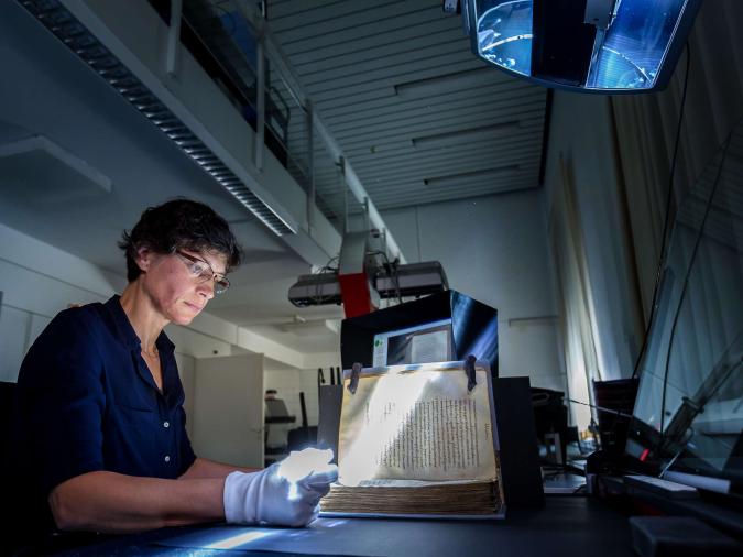 Digitalisierungswerkstatt der Bayerischen Staatsbibliothek: Eine Frau mit weißen Handschuhen digitalisiert ein historisches Buch.