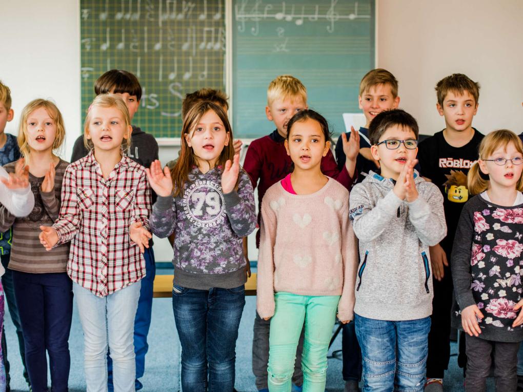 Ein Kinderchor singt vor einer Tafel im Klassenzimmer